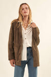 Woman wearing a brown jacket over a white shirt and blue jeans on a beige background