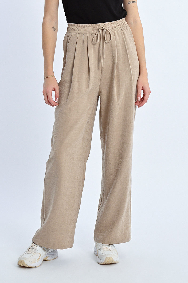 Person wearing beige wide-leg pants on a white background